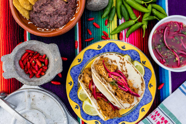 typowe meksykańskie jedzenie. stół podawany na meksykańskim obrusie z tacos z cochinita pibil, limonka, czerwona cebula, fasola z totoposem i zieloną i czerwoną papryką. - restauracja meksykańska zdjęcia i obrazy z banku zdjęć