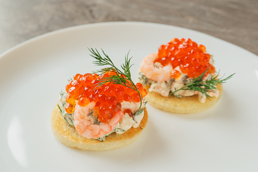 Classic Swedish appetizer - sandwiches with shrimps and caviar on white plate on dark table. Toast skagen ready to eat. Selective focus.