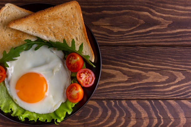 istock Fried egg with tomatoes, salad, arugula and triangle toasts on dark rustic wooden background, with right copy space. 1289600856