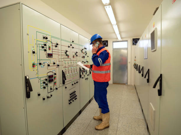 istock Worker stay in large control room. Power Plant Control Panels with schema. Engineer standing in front of the control panel, check the values and phoning with the supervisor room. 1289603060