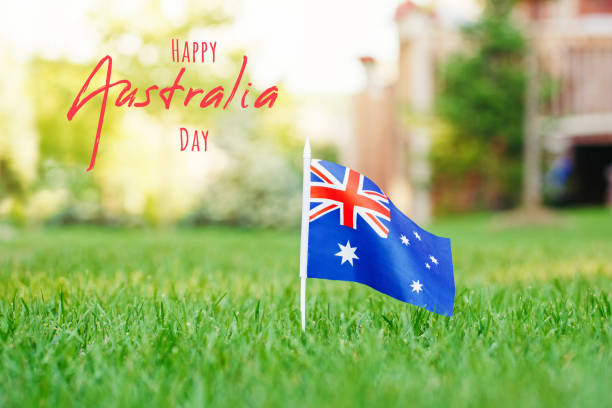 happy australia day card with greeting text. australian flag standing on green grass in front of house. australia day national holiday celebration. nature background outdoors. - australia australia day celebration flag imagens e fotografias de stock