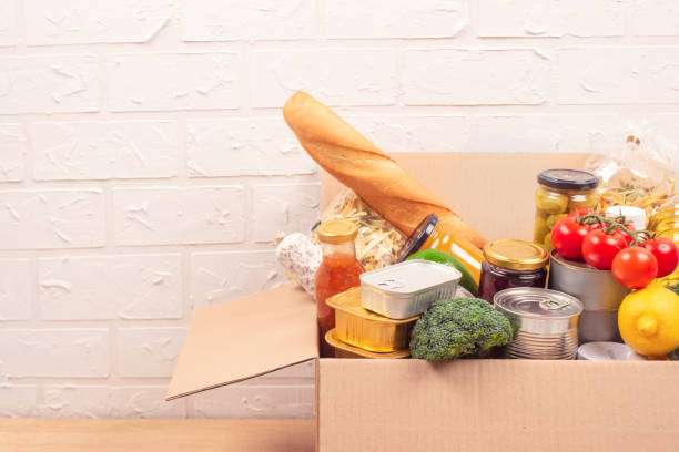 istock Donation box with different groceries, food donations on light background with copyspace - pasta, fresh vegatables, canned food, baguette, cooking oil. Food bank, food delivery concept. selective focus 1289605915