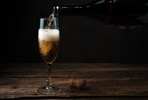 Glass in the process of filling with champagne with foam and bubbles on a wooden background. Side view. The concept of alcohol.