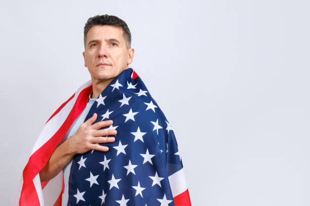 istock Handsome middle-aged man covered with American flag puts hand on his heart 1289614232