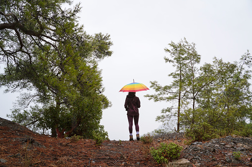 Young woman holding a colorful umbrella, hiking in forest under rain