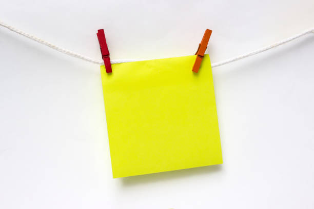 istock Close-Up Of yellow Blank Note Hanging Clothesline Against white Wall. Mock up. 1289619025