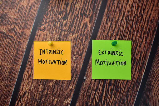Intrinsic Motivation and Extrinsic Motivation write on sticky notes isolated on office desk.