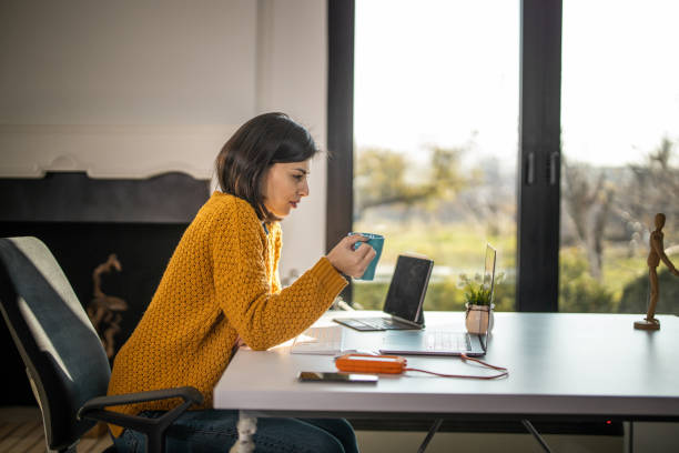 istock Woman sitting at home and working on laptop while holding coffee 1289630460