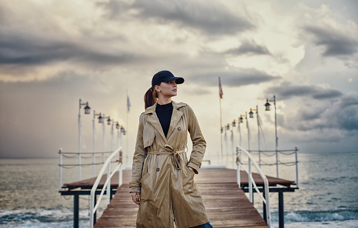 Beautiful woman in hat and coat strolling in front of the pier by the beach.