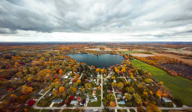 Beautiful full panoramic aerial view of the heart shaped Saugany Lake in Indiana surrounded by residential homes and autumn colored trees or foliage with fluffy white clouds in the sky above. stock photo