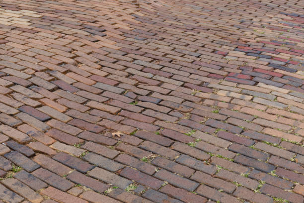 istock Mixed red brick roadway with grass growing in the cracks, running bond pattern background 1289635193