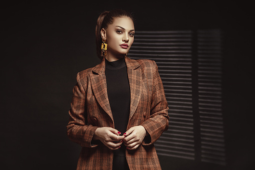 Beautiful young woman in a plaid jacket in front of a black background.