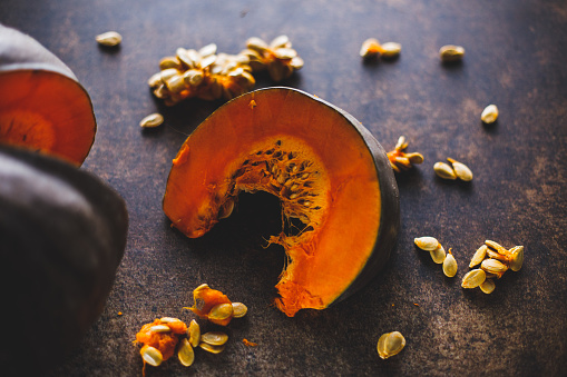 Close up shot of a slice of delicious pumpkin and abundance of it's seeds surrounding it, ready to be made into a delicious, healthy snack.