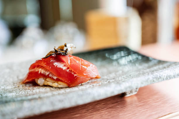 Japanese Omakase meal: Aging Raw Akami Tuna Sushi adds with sliced truffle served by hand on a stone plate. Japanese traditional and luxury meal.