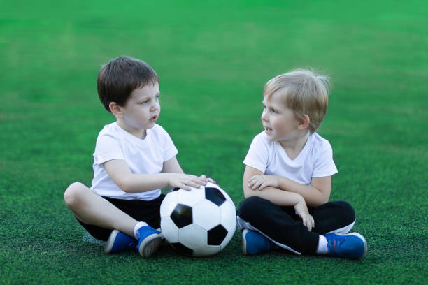 lifestyle of two children and soccer ball, sitting on grass, laughing and talking. concept about childhood, sports and communication of preschool. - outdoors playing family spring imagens e fotografias de stock