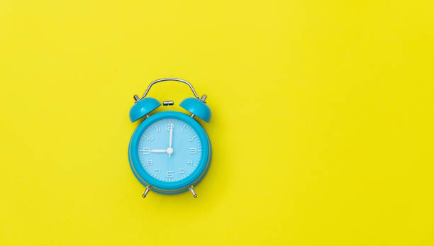 istock Blue alarm clock on yellow background 1289662487