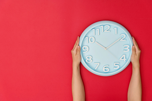 Human hand holding a clock on red background.