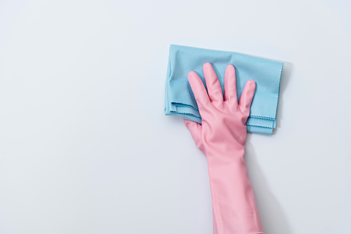 Woman hand cleaning white wall with rag.