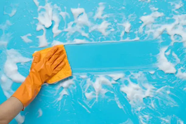 Photo of Woman hand cleaning blue wall with rag