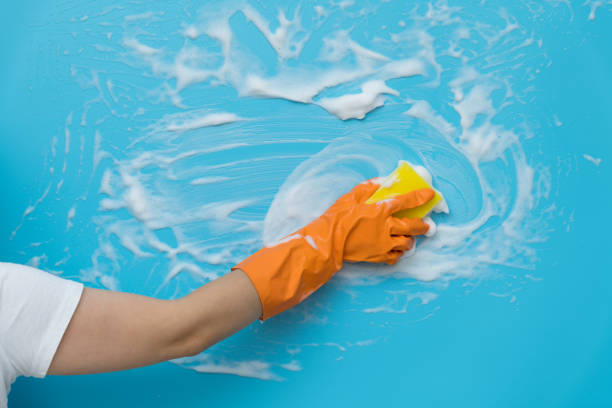 Woman hand cleaning blue wall with sponge.