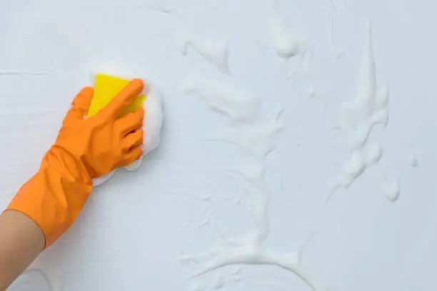 Photo of Woman hand cleaning blue wall with sponge