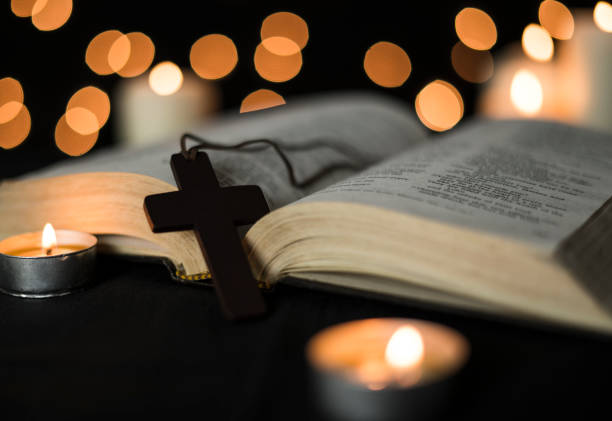 istock Cross placed on a open bible and candles against bokeh lights background 1289671142