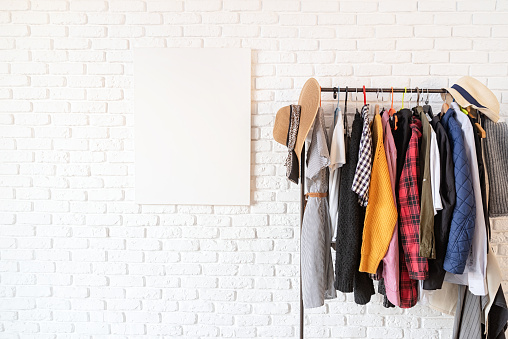 Rack with colorful clothes on hangers and frame canvas for mock up over white brick wall. Mock up design