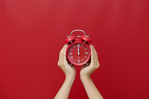 Human hand holding a alarm clock on red background.