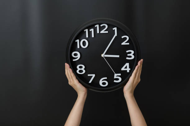 main humaine retenant une horloge sur le fond noir - clock time clock hand urgency photos et images de collection