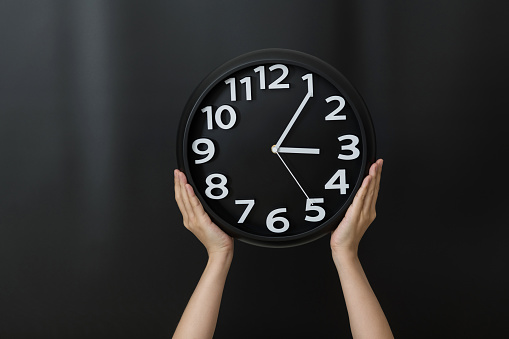 Human hand holding a clock on black background.