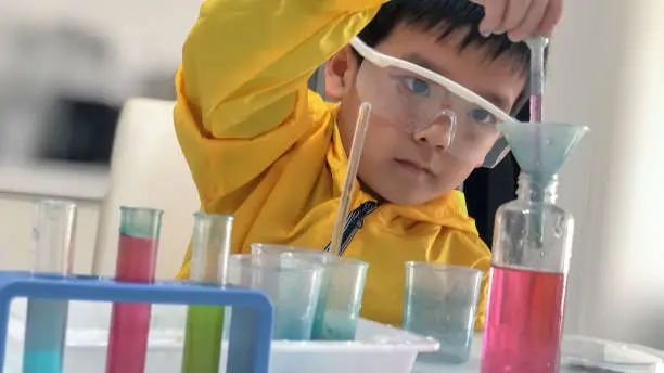 Focused asian boy learning to mix chemicals, enjoy conducting chemistry experiment