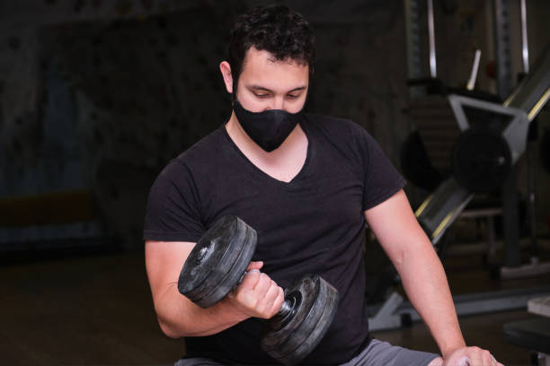 istock Strong man wearing face mask lifting dumbbells at gym 1289686837