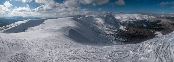 Snow and wind formed ice formations covered winter mountain plateau, tops with snow cornices in far. Magnificent sunny day on picturesque beautiful alpine ridge.