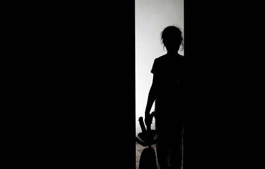 Little girl silhouette opening door into darkness, stock photo