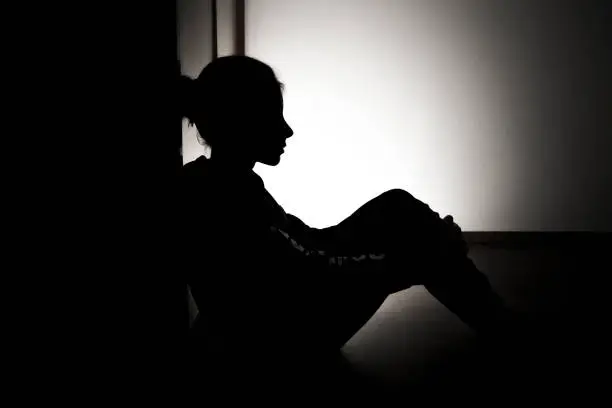 Photo of anxiety of a child concept, little girl sitting in the floor, dark room, stock photo