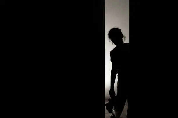Photo of Little girl silhouette opening door into darkness, stock photo
