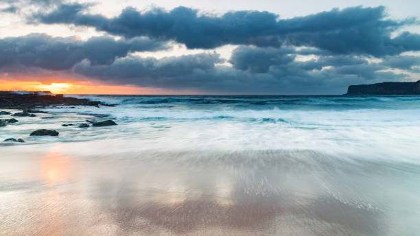 istock Grey clouds and rocky foreground overcast sunrise at the beach 1289689539