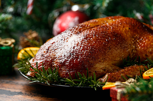 Roasted Christmas duck with decoration, gifts, green tree branch on wooden rustic table.