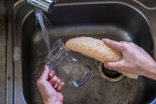 Woman hands cleaning glass cup with natural compostable loofah sponge by the sink with running tap water. Eco-friendly kitchen and home products. Zero waste sustainable plastic free lifestyle Woman hands cleaning glass cup with natural compostable loofah sponge by the sink with running tap water. Eco-friendly kitchen and home products. Zero waste and sustainable plastic free lifestyle loofah photos stock pictures, royalty-free photos & images