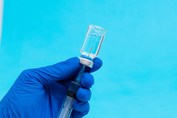 istock Doctor's hand holding syringe and vial on blue background 1289706099