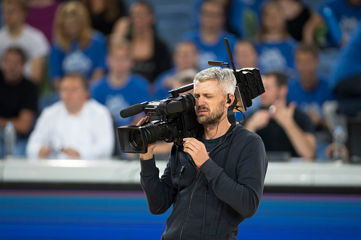 Cameraman shooting basket match in stadium.
