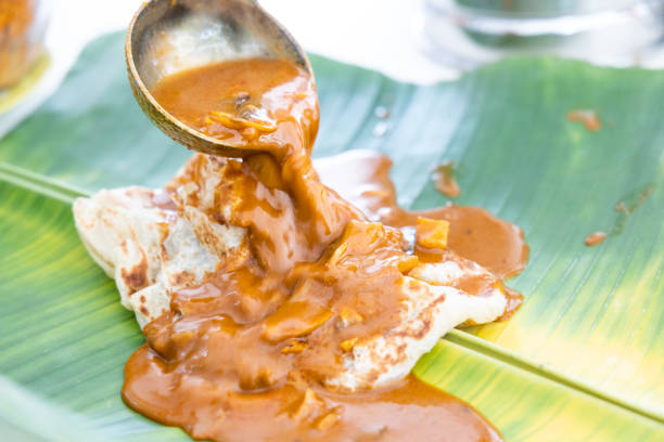 Curry being poured onto roti canai or paratha served on banana leaf Aromatic curry being poured onto roti canai or paratha served on banana leaf in Malaysia roti canai stock pictures, royalty-free photos & images