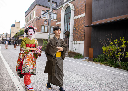 Young female tourist visiting Kyoto and experiencing Maiko (Geisha in training) makeover. Wearing traditional Japanese 'Maiko' style kimono with special white face makeup and walking around beautiful Gion district in Kyoto, Japan.