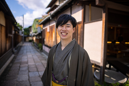 Happy young man in 'Hakama' kimono smiling on narrow street
