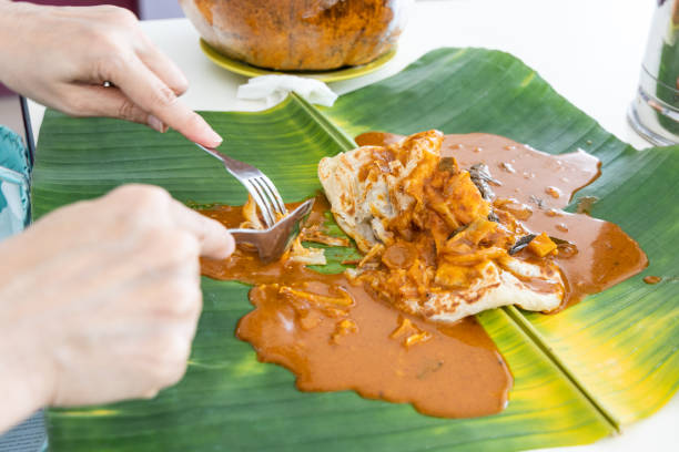 Person eating roti canai or paratha served with curry served on banana leaf Person eating roti canai or paratha served with curry served on banana leaf in restaurant roti canai stock pictures, royalty-free photos & images