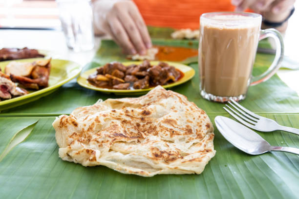 Roti canai or paratha served on banana leaf, with mutton curry and fried chicken, and popular teh tarik Roti canai or paratha served on banana leaf, with mutton curry and fried chicken, and popular teh tarik in Malaysia roti canai stock pictures, royalty-free photos & images
