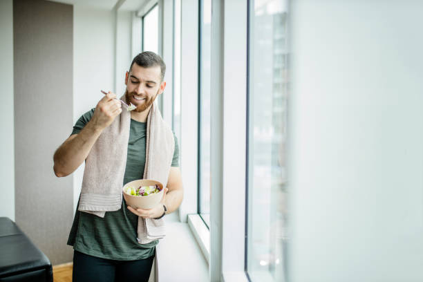 istock Young man eating fresh salad after intensive home workout 1289713381