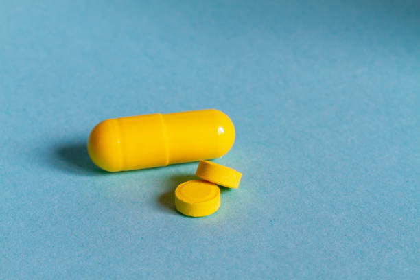 istock Yellow capsule with medicine and yellow little tablets on a blue background 1289713938