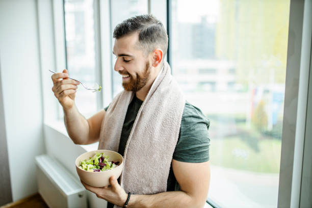 Young man eating fresh salad after intensive home workout