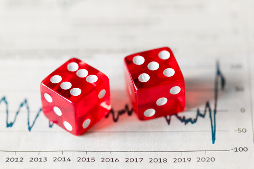 Close up macro color image depicting a pair of red dice on top of stock market data, indicating the potential risk of gambling on the stock exchange when buying stocks and shares. Room for copy space.